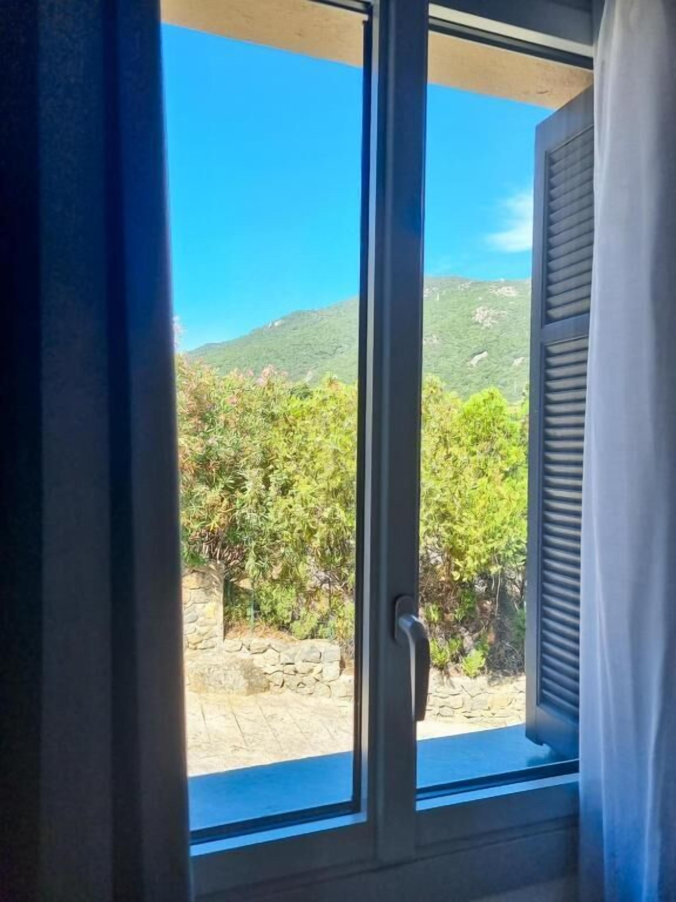 Une fenêtre donnant sur un paysage montagneux et un mur de pierre.