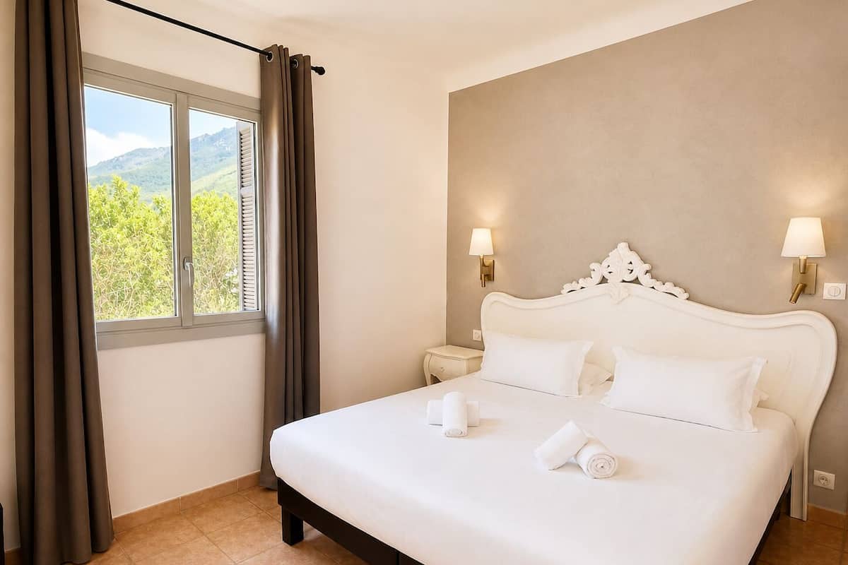 Habitación de hotel con cama, cortinas, ventana con vistas y lámparas fijadas a la pared.