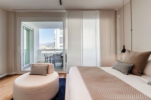 Una habitación de hotel moderna con cama, zona de estar y balcón con vistas.