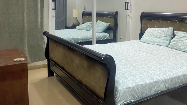 A bedroom with a bed, a wardrobe, a ceiling fan, and an air conditioning unit.