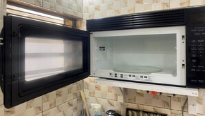 A kitchen with a microwave and oven, tiled walls, and a window.