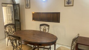 A dining area with a round wooden table, four chairs, a wall-mounted light fixture, and two framed pictures.