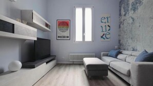 En moderne stue med et fladskærms-tv, en grå sofa, en hvid skammel og en radiator.