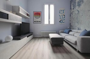 A modern living room with a flat-screen TV, a grey sofa, a white ottoman, and a radiator. - Exclusive Loft - San Siro Stadium M1 M5 Milan (Milano)