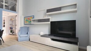 En moderne stue med et fladskærms-tv, indbyggede reoler, en lyseblå lænestol og en hvid sofa.