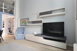 A modern living room with a flat-screen TV, built-in shelving, a light blue armchair, and a white sofa. - Exclusive Loft - San Siro Stadium M1 M5 Milan (Milano)
