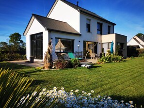 A modern two-story house with a well-maintained lawn, a patio with outdoor furniture, and a large window overlooking the garden. - 4.5 km from the beach. Beautiful, quiet house. (Saint-Lormel)