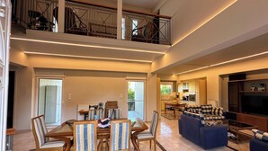 Een ruime woonkamer met een eettafel, stoelen, een bank, een televisie en een balkon met een hekwerk.