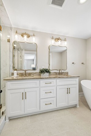 A bathroom with a white vanity, double mirrors, gold fixtures, and a freestanding bathtub. - Luxury New Build • Steps From The Beach • Pool • Sleeps11 (Destin)