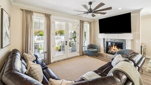 Ein Wohnzimmer mit Kamin, Ledersofas, einem Flachbildfernseher und Deckenventilator.