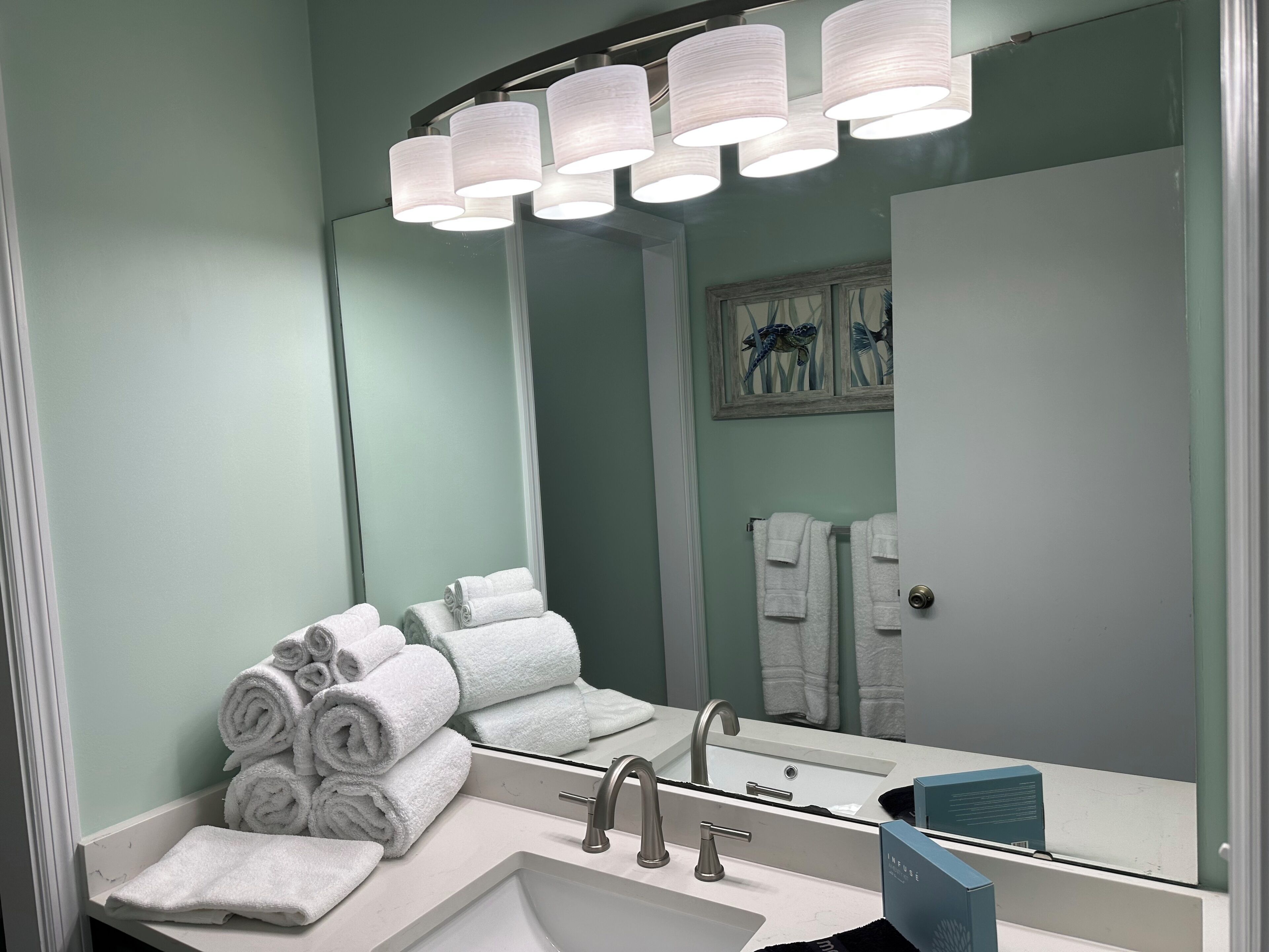 A bathroom with a sink, two faucets, a mirror, and a towel rack with rolled towels.