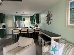 A kitchen with a central island, bar stools, a dining table, and a sofa with a starfish pillow. - Green Goddess- 2 BR townhome directly across the street from the beach. New list (Panama City Beach)