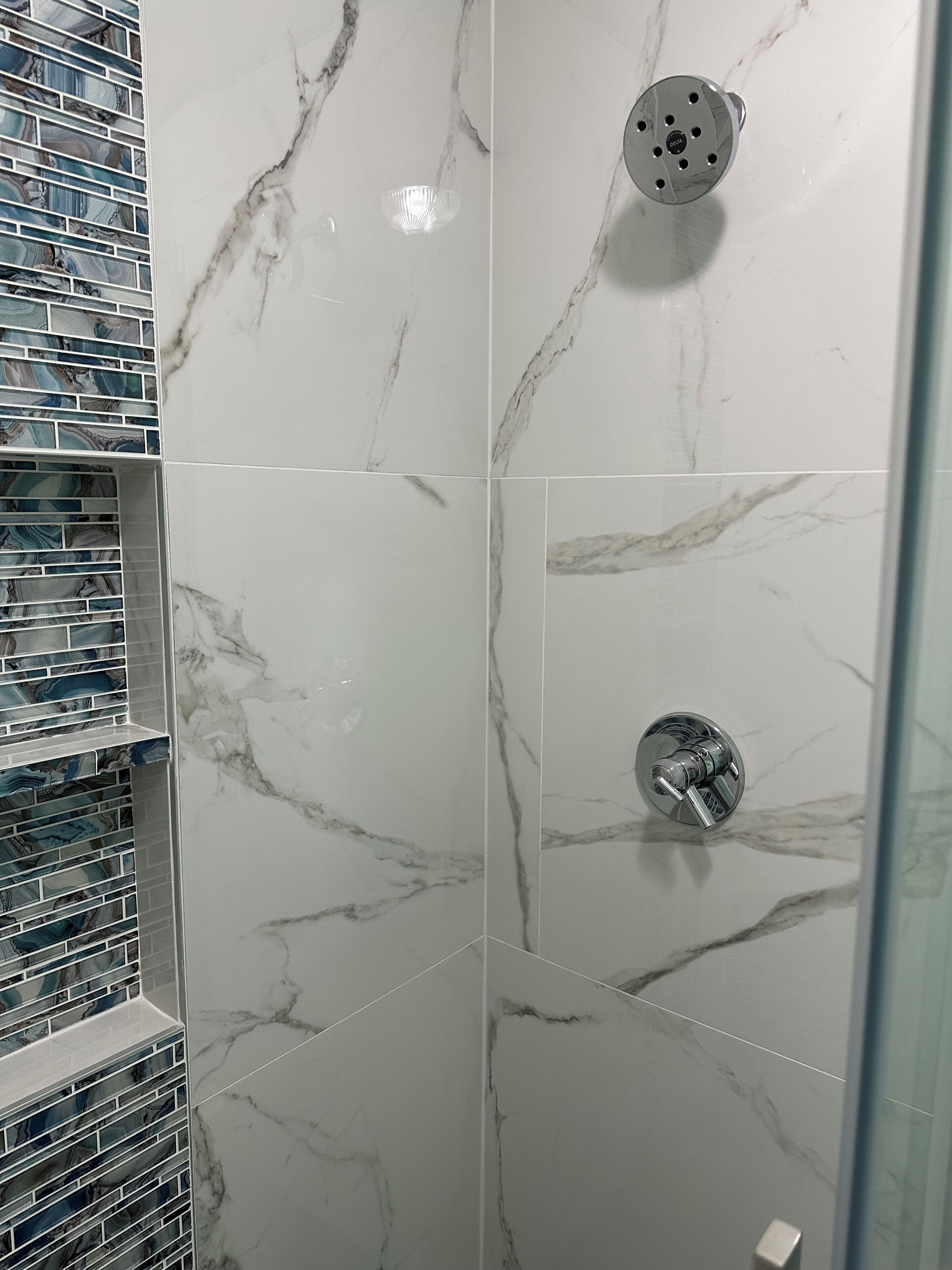 A bathroom with white marble tiles, a glass shower enclosure, and a tiled shower area.