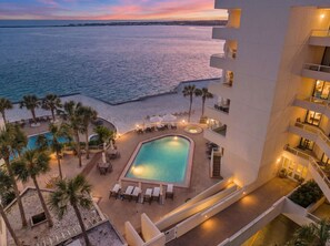 A pool area with lounge chairs and palm trees, adjacent to a building with balconies. - Best Gulf View • Private Beach • Pool + Hot Tub (Destin)