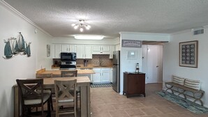 A kitchen with white cabinets, a microwave, stove, and a dining area with two wooden chairs. - Orange Beach / Cotton Bayou Waterfront / Pool / Boat Slip & Launch/Beach Access (Orange Beach)
