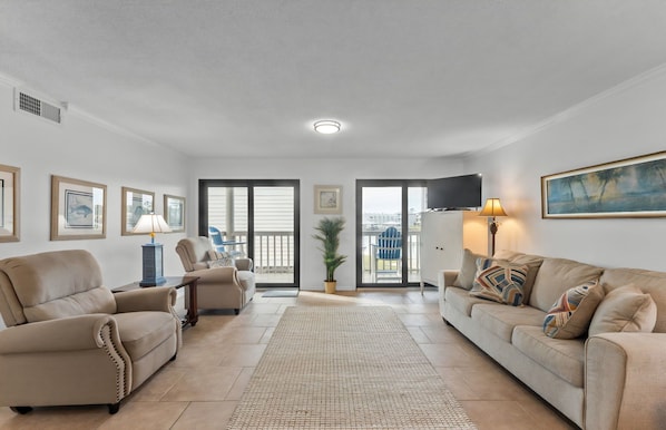 Ein Wohnzimmer mit einer Couch, Sesseln, einem Fernseher und einem Balkon mit Blick.