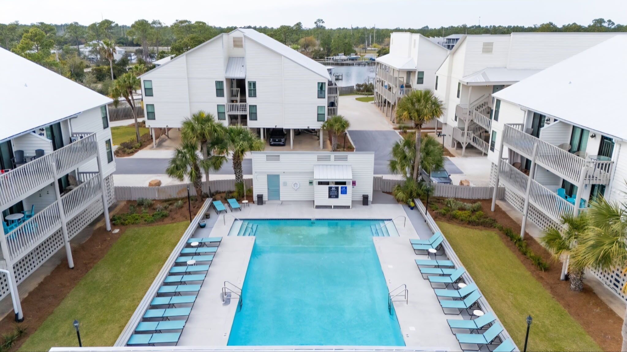 A pool area with a rectangular pool, lounge chairs, and a building with multiple balconies.
