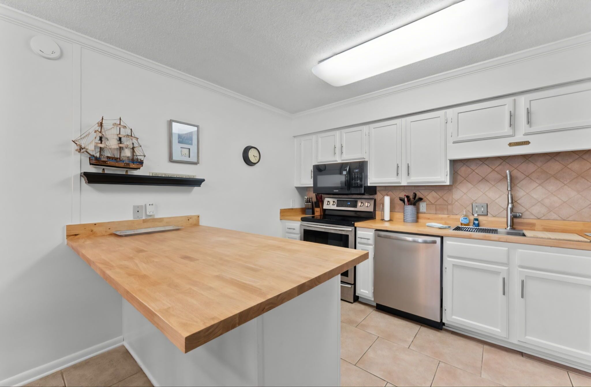 A kitchen with white cabinets, a wooden countertop, a ship model, a clock, and a microwave.