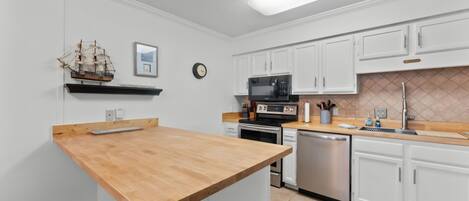 A kitchen with white cabinets, a wooden countertop, a ship model, a clock, and a microwave.