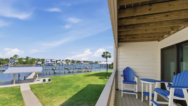 A wooden deck with blue chairs and a table overlooking a marina with boats and a water body. - Orange Beach / Cotton Bayou Waterfront / Pool / Boat Slip & Launch/Beach Access (Orange Beach)