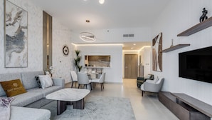 Una sala de estar moderna con un sofá, una mesa de centro y un televisor. Hay un comedor con sillas y una mesa. Se observa una cocina al fondo.