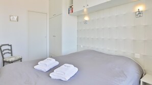 A bedroom with a bed, a chair, a wardrobe, and a headboard with lights. - Face à l'océan, Appartement avec Garage privatif (Les Sables-d'Olonne)
