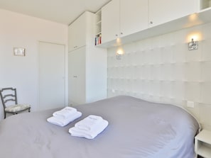 A bedroom with a bed, a chair, a wardrobe, and a headboard with lights. - Face à l'océan, Appartement avec Garage privatif (Les Sables-d'Olonne)