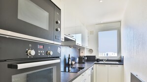 A modern kitchen with a built-in oven, microwave, and a window with a view. - Face à l'océan, Appartement avec Garage privatif (Les Sables-d'Olonne)