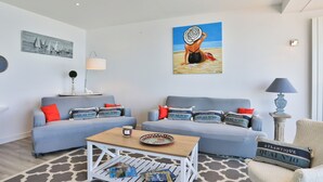 A living room with two sofas, a coffee table, and a chair. There are paintings on the walls and a lamp on a side table. - Face à l'océan, Appartement avec Garage privatif (Les Sables-d'Olonne)