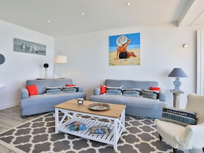 A living room with two sofas, a coffee table, and a chair. There are paintings on the walls and a lamp on a side table. - Face à l'océan, Appartement avec Garage privatif (Les Sables-d'Olonne)