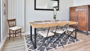 A dining area with a wooden table, chairs, a rug, a chair, a cabinet, and a mirror on the wall. - Face à l'océan, Appartement avec Garage privatif (Les Sables-d'Olonne)