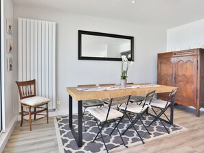 A dining area with a wooden table, chairs, a rug, a chair, a cabinet, and a mirror on the wall. - Face à l'océan, Appartement avec Garage privatif (Les Sables-d'Olonne)
