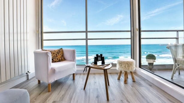 A room with a large window overlooking the ocean, a white sofa, a small table with binoculars, and a wicker chair. - Face à l'océan, Appartement avec Garage privatif (Les Sables-d'Olonne)