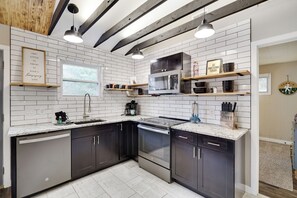 A modern kitchen with white subway tiles, dark cabinets, stainless steel appliances, and wooden beams. - Harmony Hideaway- Your Perfect Pocono Retreat-Pet Friendly with Hot Tub (Lake Harmony)