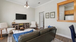 A living room with a sofa, chairs, a television, a wooden cabinet, and a mirror. - Full apartment rental with a balcony downtown. Park and walk to everything. (Ocean Springs)