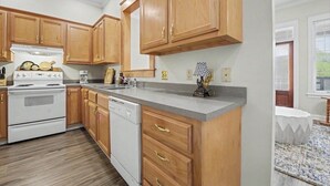 A kitchen with wooden cabinets, a white stove, a dishwasher, and a granite countertop. - Full apartment rental with a balcony downtown. Park and walk to everything. (Ocean Springs)