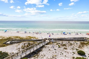 Ein Strand mit einer Holzpromenade, die zum Wasser führt, Sand und Sonnenschirmen.
