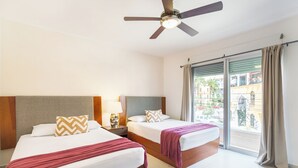 A hotel room with two beds, a ceiling fan, a nightstand with a lamp, and a view of the outside. - Apartment central 8 pax tendenza, 2 rooms and with services included. (Playa del Carmen)