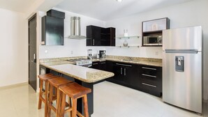 A modern kitchen with a central island, black cabinets, stainless steel appliances, and wooden stools. - Apartment central 8 pax tendenza, 2 rooms and with services included. (Playa del Carmen)