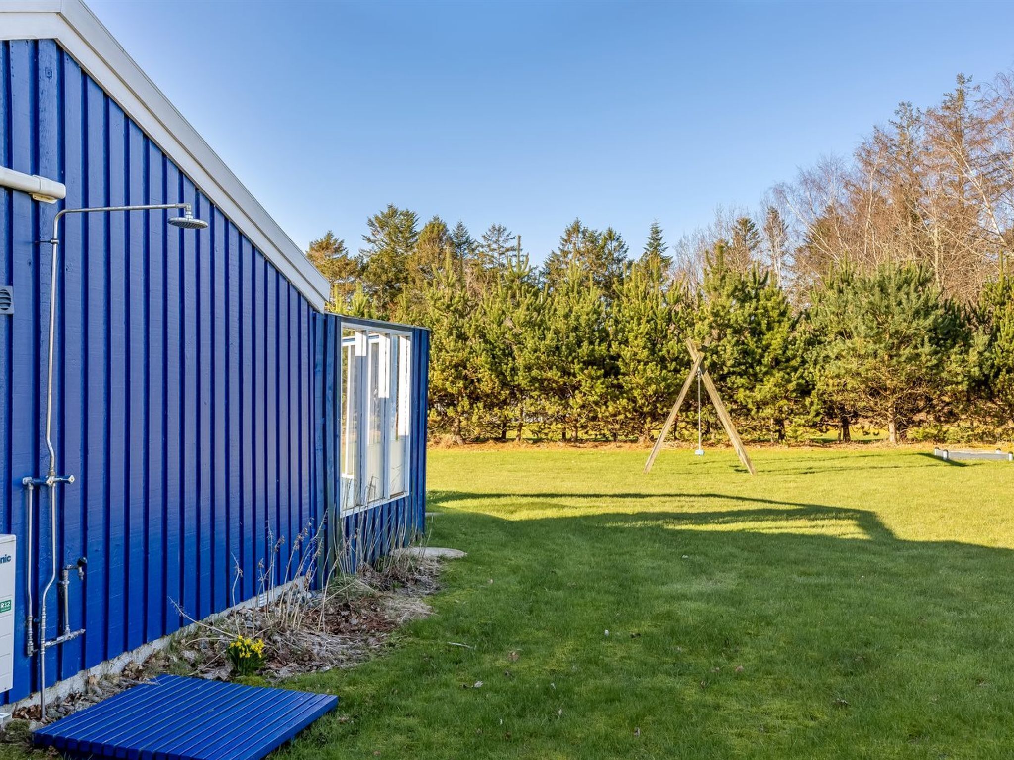 A blue building with a window, a grassy yard, and a swing set.
