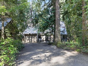 Una cabaña con entrada de grava, rodeada de un bosque denso.