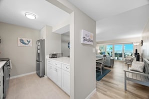 Eine moderne Küche mit weißen Schränken, einem Kühlschrank und einem Toaster. An der Wand hängt ein Schild mit der Aufschrift 'Hello Sunshine'.