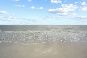 Ein Strand mit ruhiger Wellenbewegung, blauem Himmel und weiter Ferne.