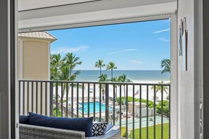 Ein Balkon mit Blick auf einen Strand, ein Schwimmbad und Palmen.