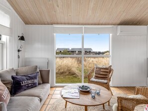 Ein Zimmer mit einer Couch, einem Korbsessel, einem Couchtisch und einem großen Fenster mit Blick auf Gebäude und Rasen.