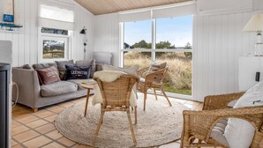A room with a grey sofa, wicker chairs, a round rug, and a large window with a view of the outdoors. - "Enni" - 350m from the sea by Interhome (Skagen)