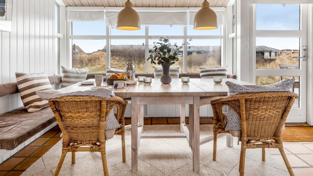 A room with a wooden ceiling, large windows, wicker chairs, a table with a vase, and a view of the outdoors. - "Enni" - 350m from the sea by Interhome (Skagen)