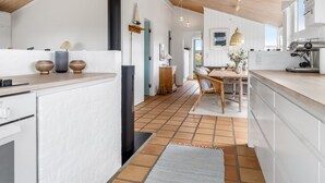 A modern kitchen with white cabinetry, a wooden ceiling, and a dining area with a table and chairs. - "Enni" - 350m from the sea by Interhome (Skagen)