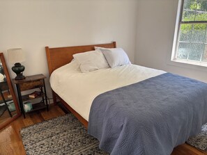 Ein Schlafzimmer mit einem hölzernen Bett, weißer Bettwäsche, einer blauen Decke, einem Nachttisch mit Lampe und einem Teppich.
