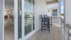 Un balcón moderno con puerta corredera de vidrio, piso de madera y vista a una zona residencial.